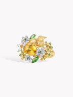 Gold cocktail ring with yellow oval gemstone, white diamond cluster, green leaf accents