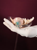 Gemstone pendant necklace on a gloved hand, teal emerald-cut center with diamond halo