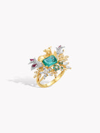 Gold gemstone ring featuring teal emerald-cut center, branching accents, and purple side stones