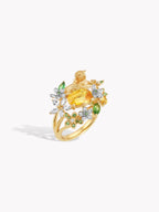 Gold ring with yellow oval center stone, white diamonds, green accents, garden motif