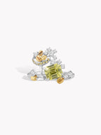 Silver gemstone ring with green center stone, scattered clear stones, and gold-tone flower motifs