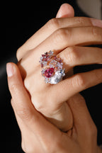 Open ring on hand with silver-tone band, pink pear center stone and floral gem cluster