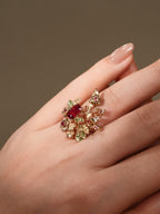 Gold-tone branch ring on fingertip, with maroon square center and colorful gemstones