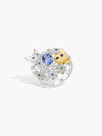 Silver ring with oval blue sapphire center, small cat faces, floral cluster prongs