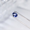 Oval royal blue sapphire gemstone in silver-tone prong setting, close-up
