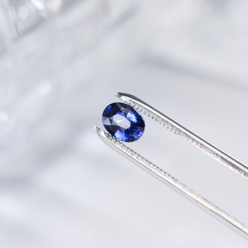 Oval royal blue sapphire gemstone in silver-tone prong setting, close-up