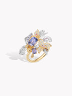 Gold band floral ring with oval blue center stone, surrounded by clear pavé details