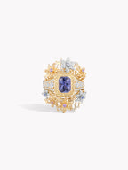 Gold-toned gemstone ring with purple sapphire center and diamond-like halo accents