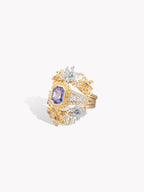 Gold-toned ring with purple sapphire center surrounded by diamond-like clusters, side view