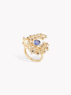 Gold-tone ring with oval blue sapphire center and diamond-like floral halo, side view