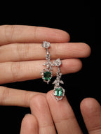 Diamond-studded drop earrings with emerald-green square center and dangling teardrop