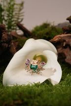 Gold ring with teal emerald-cut center, clear and pink gems, resting on white flower