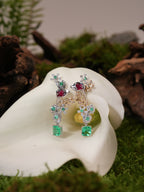 Floral drop earrings on ear, with emerald-green square stones, red centers, and green crystal drops