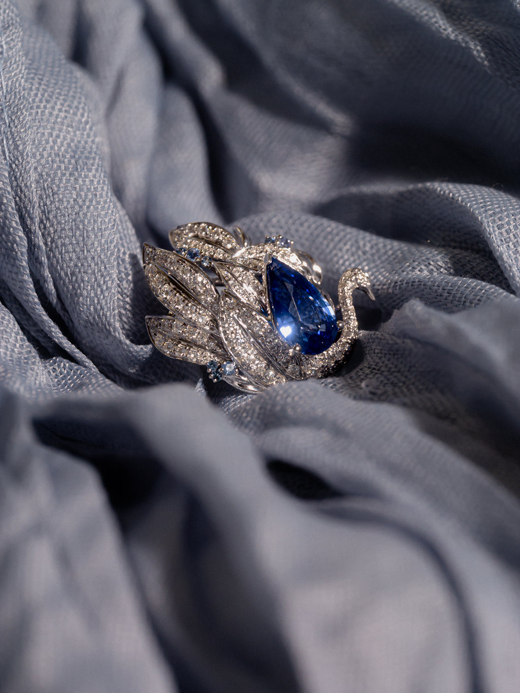 Swan sapphire ring on fabric: oval blue center stone with sparkling crystal settings