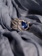 Swan sapphire ring on fabric: oval blue center stone with sparkling crystal settings