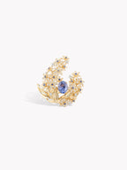 Gold-tone ring with blue sapphire center and diamond-like floral halo, angled front