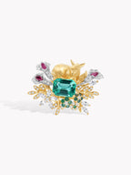 Gold ring with teal emerald-cut center, floral prongs, clear stones, and magenta gems