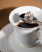 Oval blue gemstone ring with gold prongs and silver flower accents with clear stones